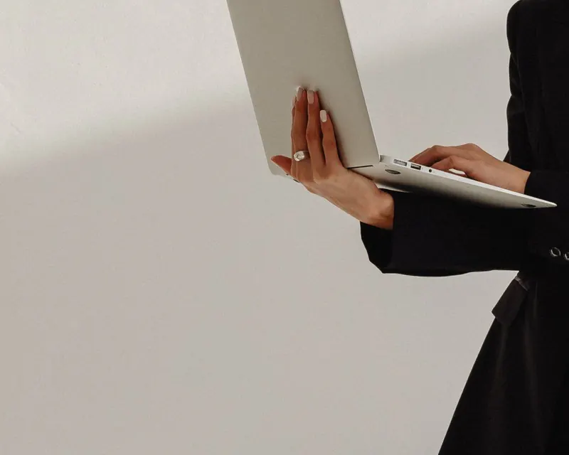 A woman in a black blazer holding an open laptop