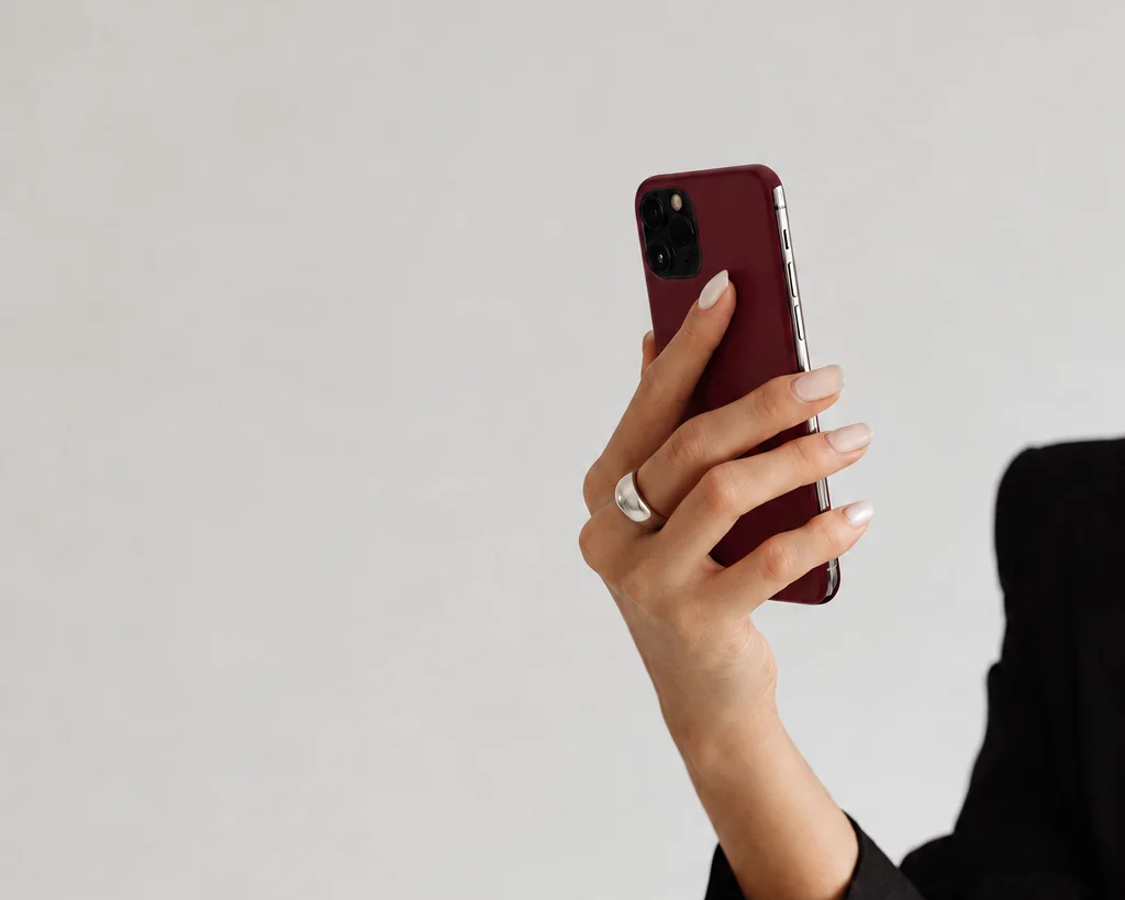 A hand with a silver ring holding up a burgundy iPhone