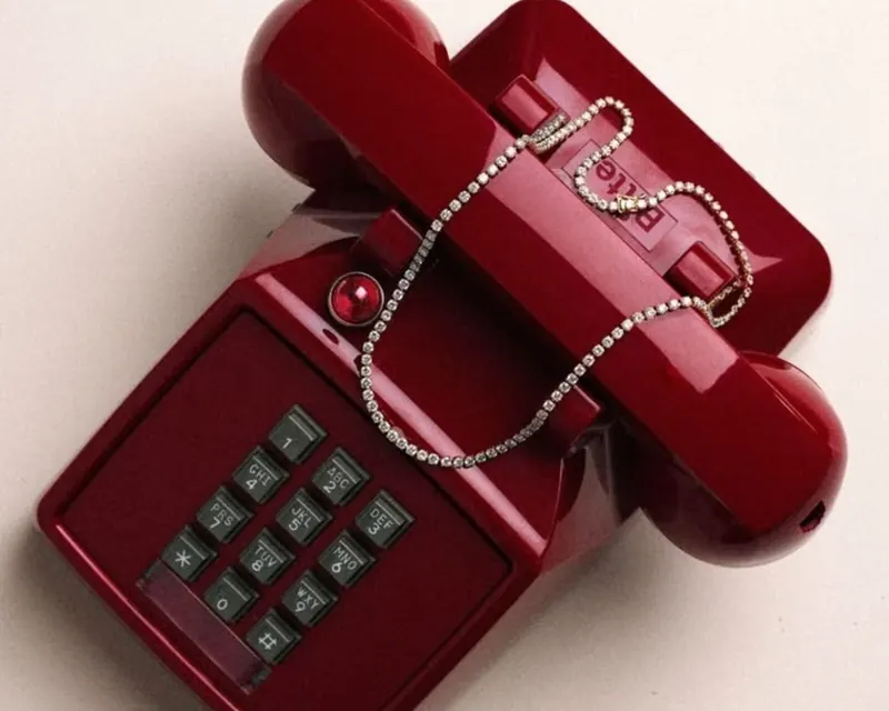 A red vintage telephone draped with a diamond necklace