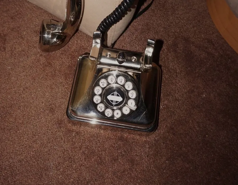 A vintage chrome rotary telephone resting on a brown carpet